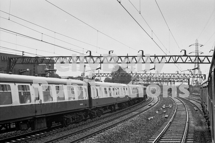 LPPC DSL BW 0430 
 A miserable wet Sunday lunchtime on the Queensville Curve, Stafford sees two trains of Mark 1 stock passing during the first weeks of September in the mid-1970s. Early enough for some summer dated trains to still be running and the shot is taken from a holiday service operating on British Rails South West/North East axis, now referred to as Cross Country. Going away from the camera on the left, up, main line is a Sunday service heading for London with a Class 86 at its head. No doubt having been, or about to be, diverted, the trains passengers  not customers  are probably beginning to wonder if they will ever reach their destinations. Our train has arrived at this point by coming via the Lickey Incline route to Birmingham New Street and then reversing. Heading out by way of the South to East curve at Soho, it has headed for Walsall continuing onto what was then the freight-only line through Ryecroft Junction, across Cannock Chase and joining the West Coast main line at Rugeley. This was rare mileage at this time, with enthusiasts travelling on most services that were diverted onto non-passenger routes on Sundays.