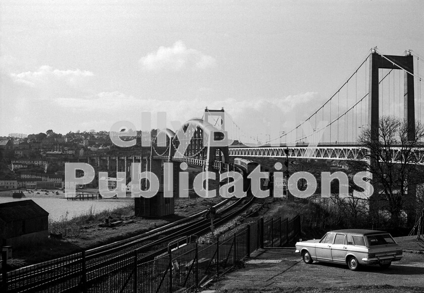 LPPC DSL BW 0399 
 It is low tide at Saltash as the first passenger train of the day from Penzance, on a Sunday morning in 1973, proceeds cautiously towards journeys end at Plymouth over Brunels magnificent Saltash Bridge. Consisting of one of the earlier Swindon-built Cross Country DMU sets, the train faces the rare sight of a Ford Zodiac Mark 4 Estate Car by Abbots of Farnham. 
 Keywords: BR, 1973, Plymouth, Saltash Bridge, Western, Class 119, DMU, Passenger