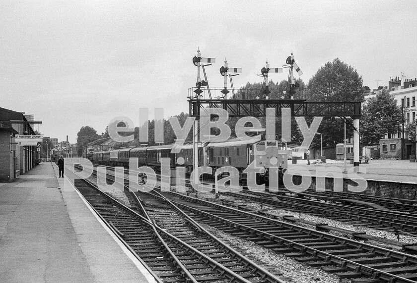 LPPC DSL BW 1273 
 One day the Special Carriage Notices landed on my desk and foremost was a very small item. It consisted of only three lines of print. The Royal Train was due to arrive at Kensington Olympia that Sunday in the early afternoon. In theory it had nothing to do with us as the train was due onto the WR at North Pole, run briefly to Kensington, where the locos would run round, and it would then depart northwards again. One big attraction was that this was not the latest Royal Train, but the previous incarnation, thus it contained such gems as the 12-wheeled converted ex-LNWR power car, which can clearly be seen as the first vehicle behind the two Sulzer Type 2 Class 25s. Other than the railway employee on my platform and the member of the public in the right background, there was no-one else around to record the movement. 
 Keywords: BR, Class 25, Double Header, Royal Train, Kensington Olympia, ECS, Western