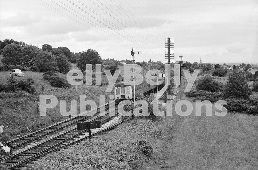 LPPC DSL BW 1268 
 Waiting at Malvern Wells westbound outer home signal is a three-car Birmingham area WR DMU which has probably formed a Birmingham New Street to Great Malvern stopper via Stourbridge Junction. It will soon draw forward across to the up line to return to Great Malvern to form a service back to New Street. It is some time since the goods loop was last used as there were no longer any booked freight trains running between Worcester and Hereford. The LMS branch to Upton upon Severn and Ashchurch diverged in the far background, just before the loop turnout. The line then ran behind the bushes to the right, to Malvern Hagley Road station which was out of sight behind and to the right of the photographer. 
 Keywords: BR, Western, DMU, Malvern Wells, Passenger