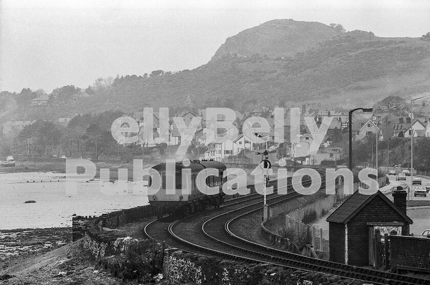 LPPC DSL BW 1159 
 Interlude at Llandudno Junction 6 a Class 103 Park Royal DMU makes it way to Llandudno having just departed from LLandudno Junction station. The fascinating features of this photo are not directly related to the train. The background is dominated by the Great Orme, which enjoys a tramway to its summit. The platelayers hut appears to have an outside privy, and the collection of cars on the A546 include a Mk2 Ford escort, a Morris 1300, a Cortina Mk3 with twin headlights, a Triumph Spitfire and what could be a Morris Marina.... True 1970s nostalgia! 
 Keywords: Digital, ISO, John Stiles